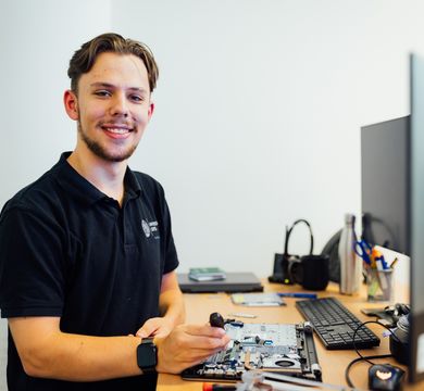 ein Mann steht vor zwei Bildschirmen und schraubt am einem Laptop herum