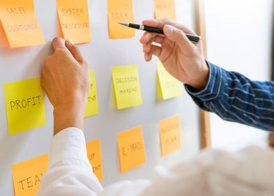 Zwei Menschen zeigen auf Post-it-Zettel an einem Whiteboard